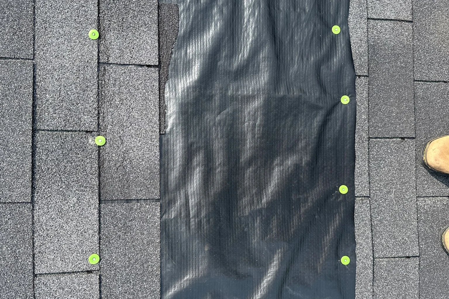 Black temporary tarp secured over roof shingles